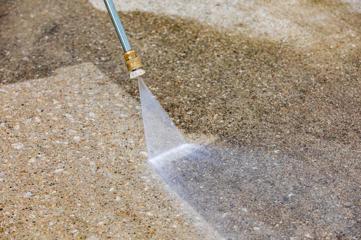 Close-up of a pressure washer wand cleaning dirty concrete and revealing a clean path